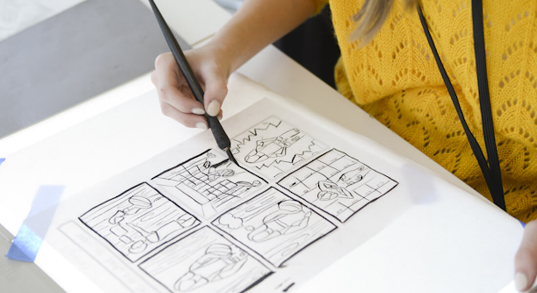 person working with ink on a light panel for a comic strip